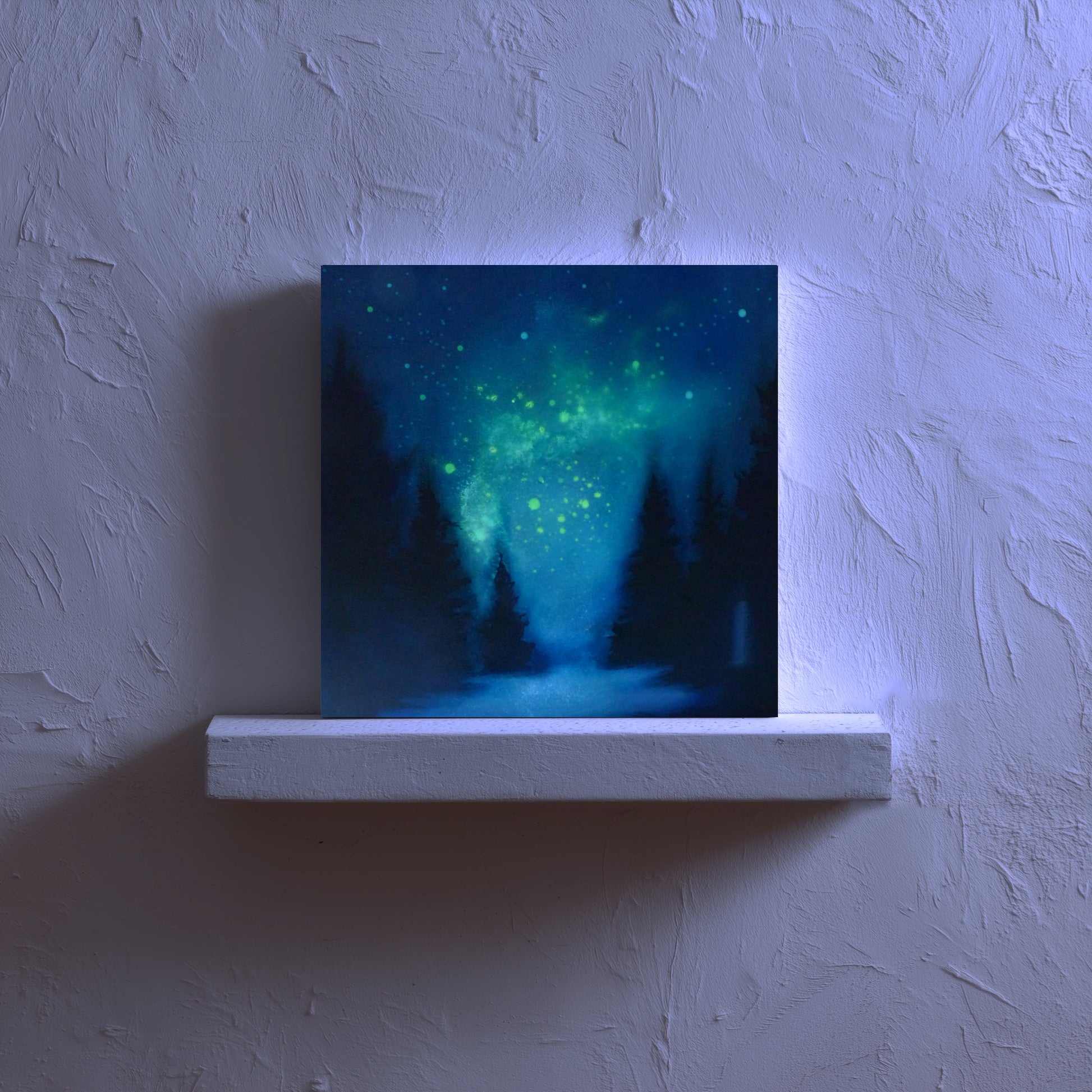 painting of a forest under a glow ing starry night sky on a white ledge against a textured wall.
