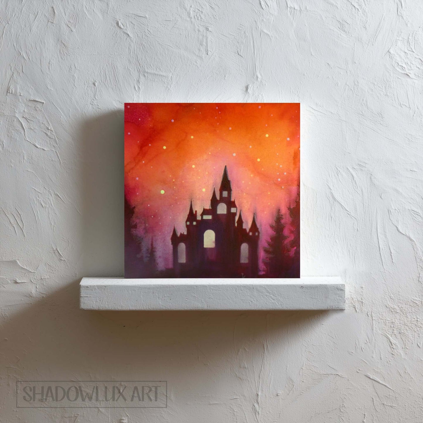Artistic depiction of a castle silhouette against a vibrant orange and pink sky on a white shelf.