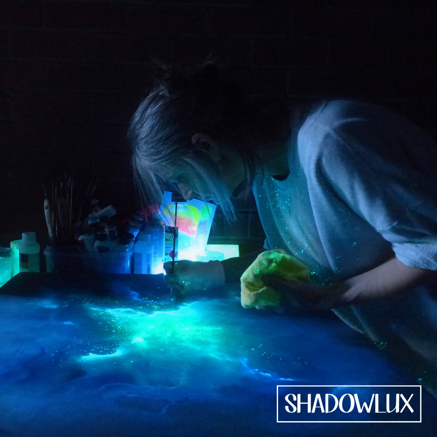 Person painting a glowing nebula artwork in a dark setting.