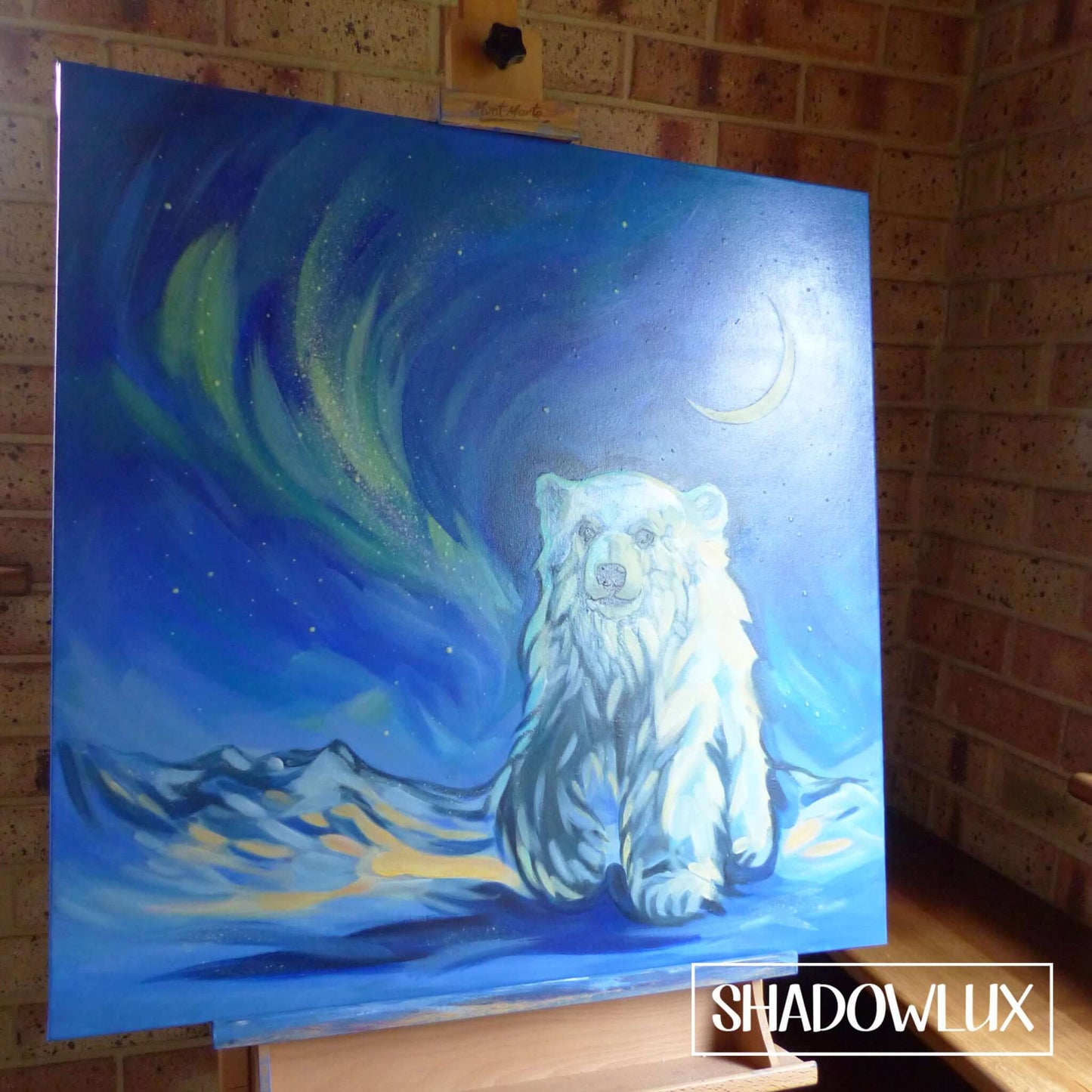 glow painting featuring a snow bear and crescent moon and aurora, resting on an artists easel