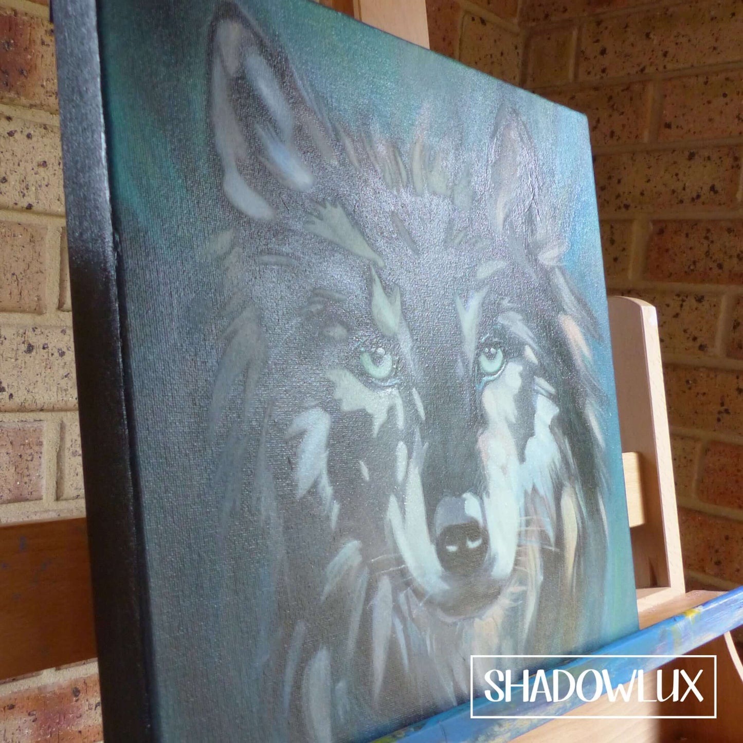 Hand-painted glow in the dark wolf portrait on canvas displayed on an artist’s easel
