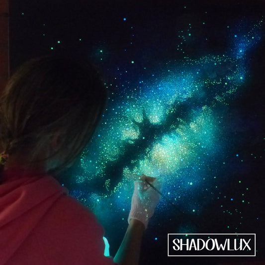 artist painting a starry night sky artwork that is glowing in the dark 