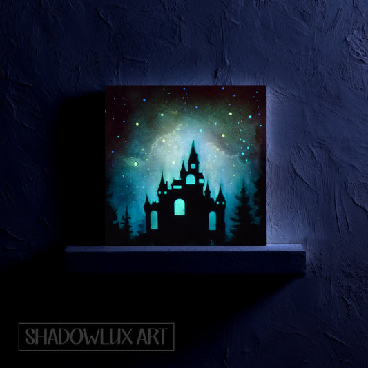 Glow in the dark artwork of a castle silhouette with a glowing blue sky on a dark background, credited to Shadowlux Art.