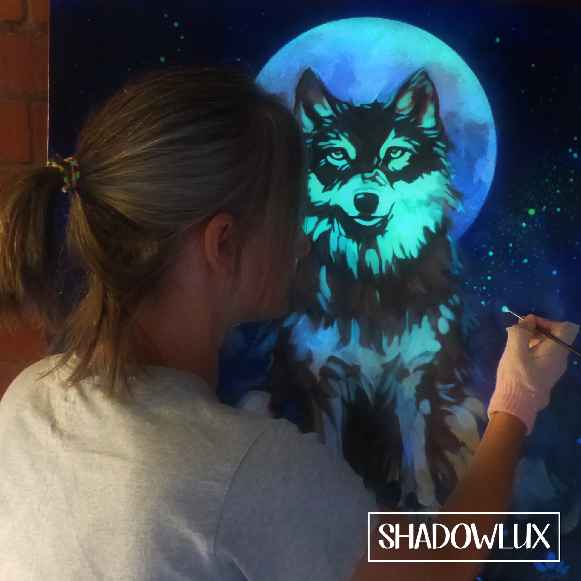 Artist Esther Iranyi painting a glow in the dark wolf with a blue moon and starry sky